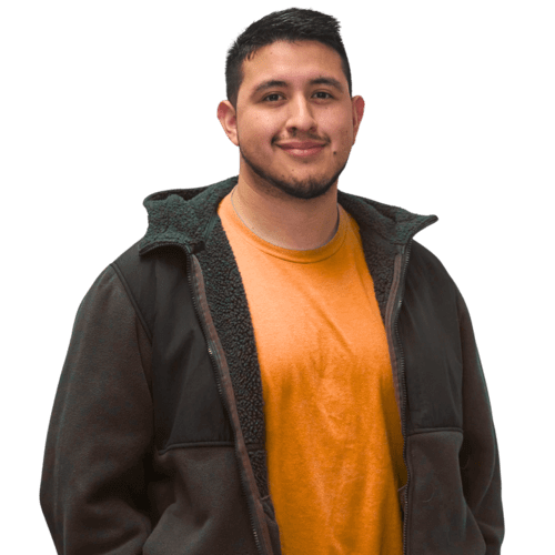 A man wearing an orange shirt and jacket stands confidently and smiling towards the camera.